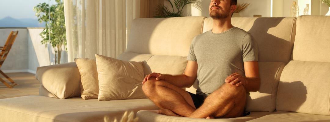 Mann zu Hause meditieren tun Yoga Übungen sitzen auf einer Couch und atmen frische Luft bei Sonnenuntergang