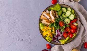 Grilled Chicken Mango Salad with cilantro, cucumbers, cherry tomatoes and red onion, top view with copy space