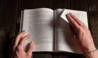 Nahaufnahme männlicher Hände, die eine Seite eines Buches auf einem dunklen Holztisch drehen. Konzept von Lesen, Literatur, Bildung, Lernen und Wissen