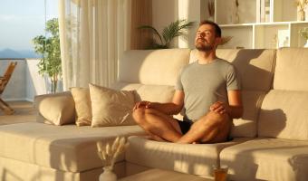 Mann zu Hause meditieren tun Yoga Übungen sitzen auf einer Couch und atmen frische Luft bei Sonnenuntergang